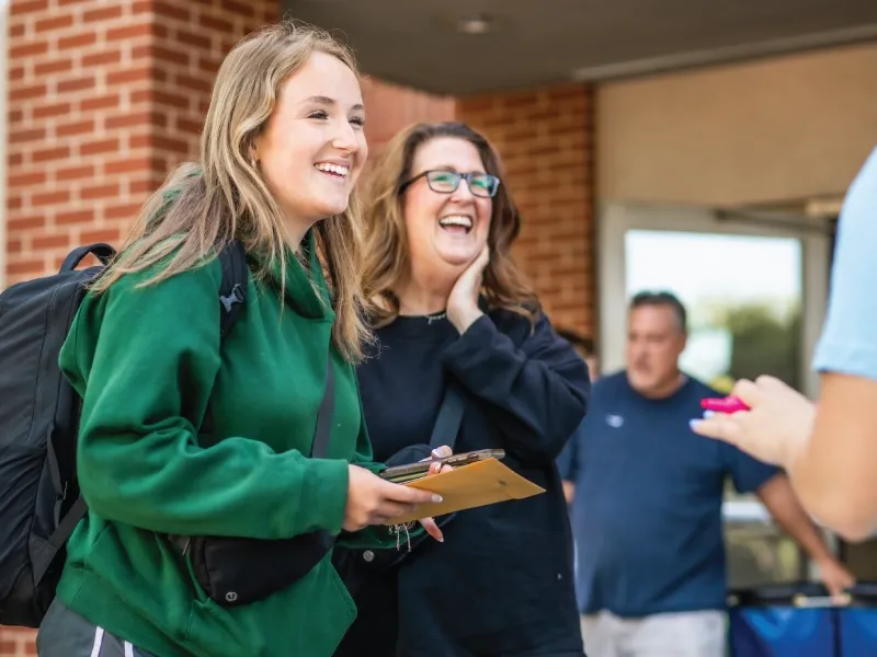 Student smiling with a parental figure outside